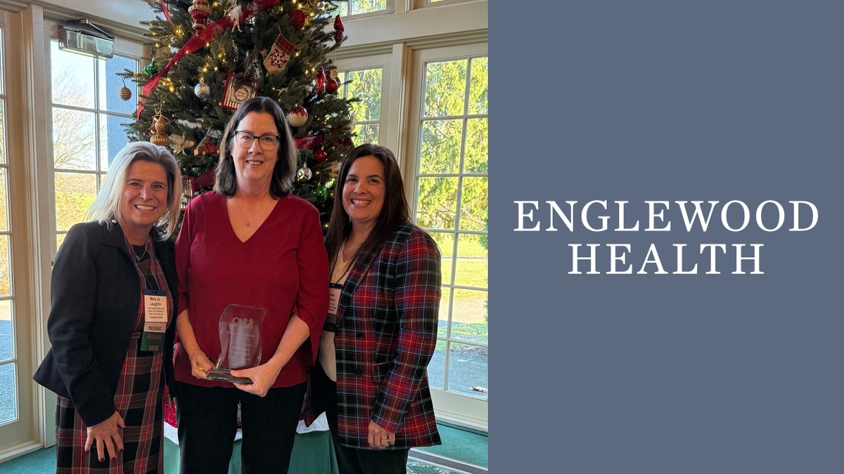 three women standing in front of Christmas tree. the woman in the middle is holding an award.