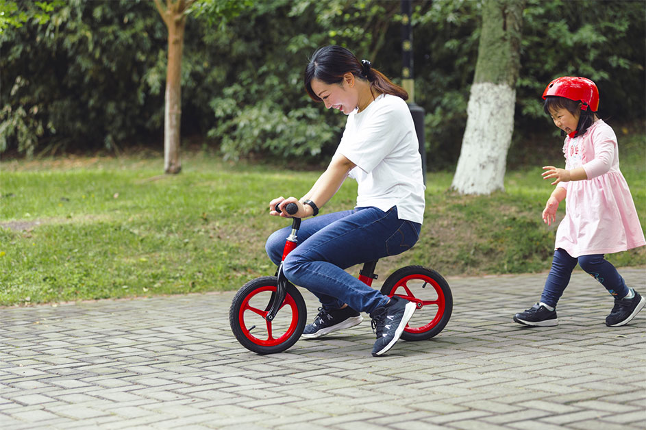 Asian woman young mother ridding bike with her daughter little girl running after behind in the summer park